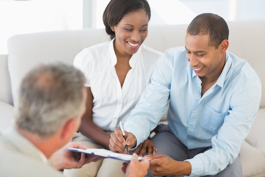 Young smiling couple signing contract on the couch in the office